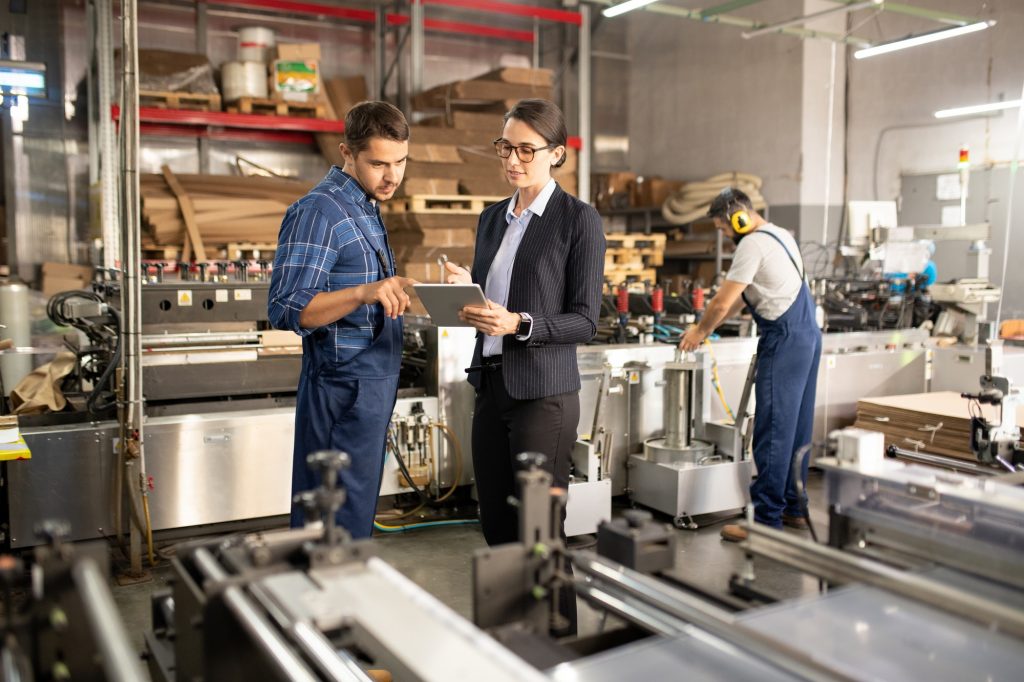 Two young confident workers of processing factory discussing online data